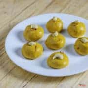 7 Easy And Quick Vrat And Upvas Recipes Besan Ke Laddu on a white plate with some cashew and saffron used to garish the laddu kept on a wooden surface
