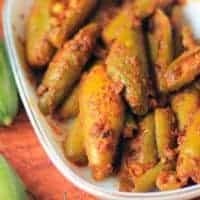 How To Make Parwal Ki Sabzi - Bharwa Parval Recipe Bharwa Parval on a white bowl putted on a dark coloured surface with some green chili and some parval on the background |