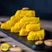 7 Easy And Quick Vrat And Upvas Recipes Nariyal ki barfi on a black plate with some almonds and pictachios