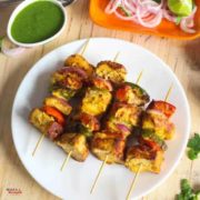 21 Paneer Recipes in Hindi - पनीर व्यंजन हिंदी में Paneer Tikka on a white plate with some green chili ,lemon and onion rings with some green chutney