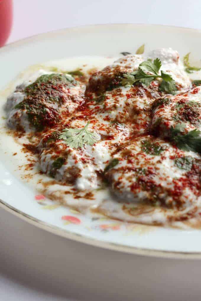 Dahi Vada on a white plate garnished with red chilli powder coriander leaves 