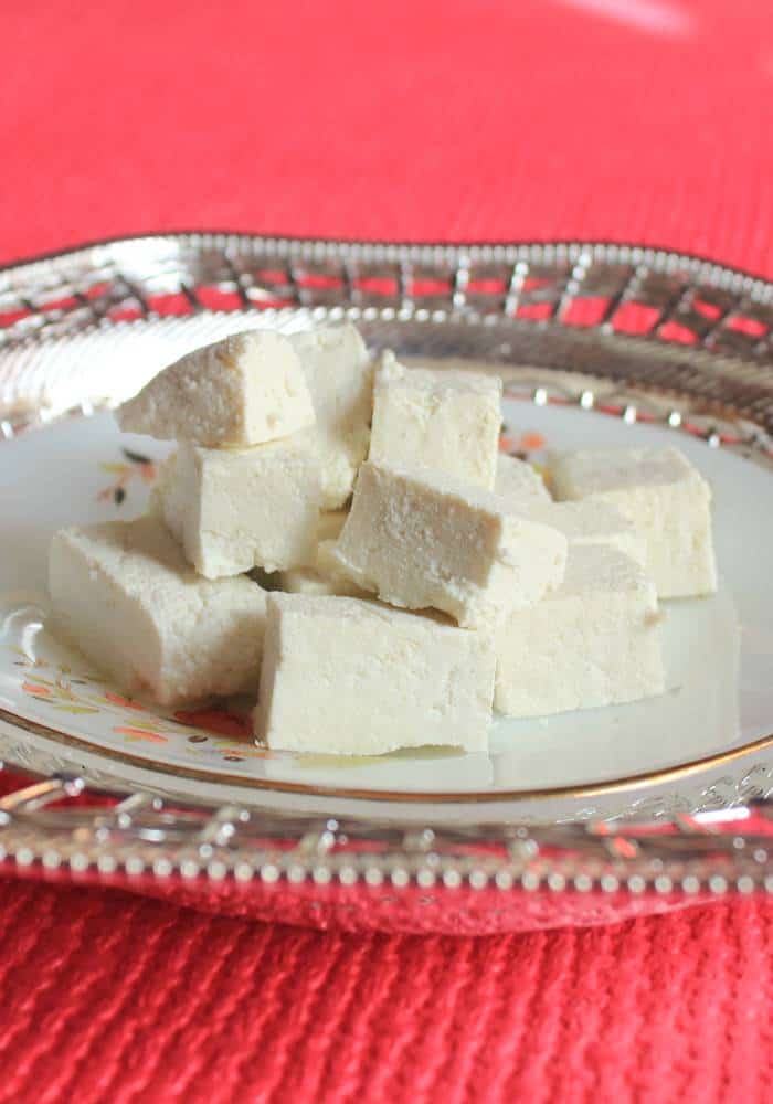 Paneer cutted into cubes on a silver coloured plate with a red background| 