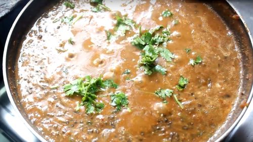 Dal Makhani on a deep heavy pan on a white surface. garnished with butter and cream with some coriander leaves | www.mintsrecipes.com |