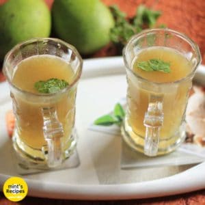 Aam Ka Panna on a transparent glass with some mints leaf keeped on a white tray with some raw mango on the background |