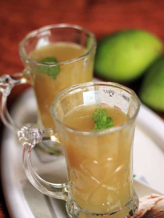 Aam Ka Panna on a transparent glass with some mints leaf keeped on a white tray with some raw mango on the background |