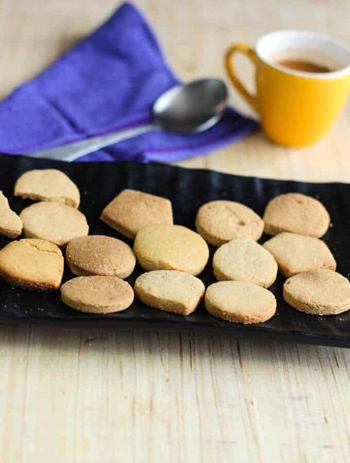 Atta Cookies on a black plate with some coffee in the cup with a spoon