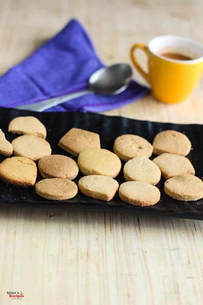 Atta Cookies on a black plate with some coffee in the cup with a spoon