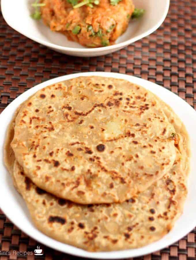 Aloo Parantha | On a white plate with some aloo paratha's kept on a dark color mat and some potato mixture on a white bowl.