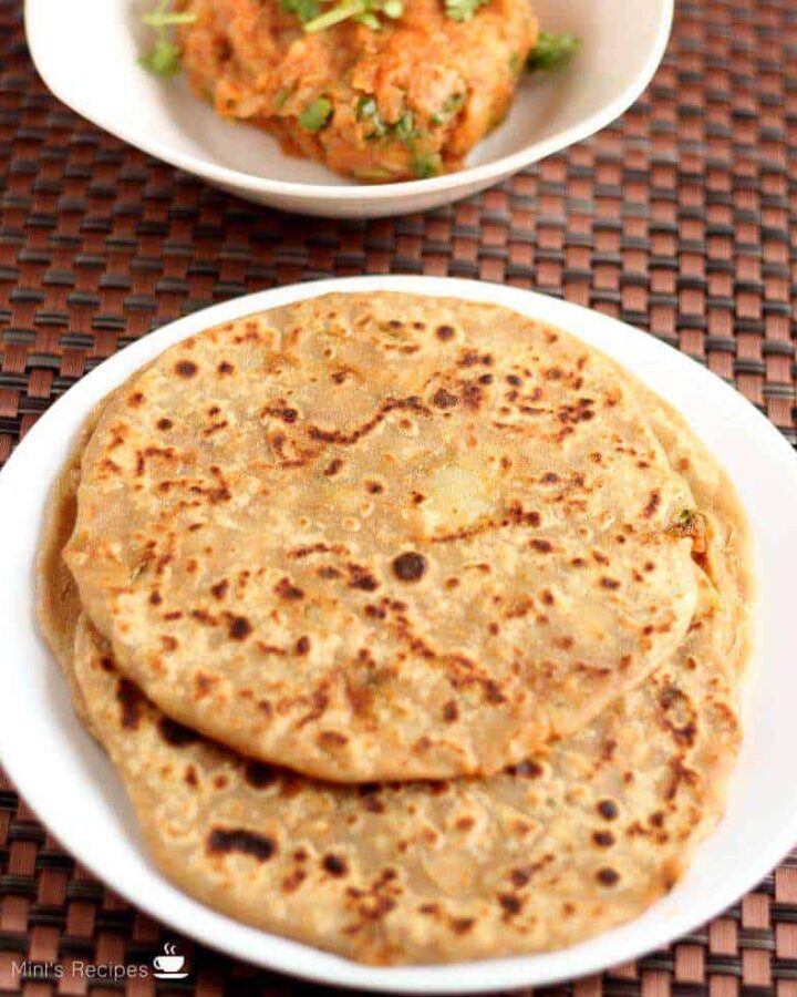 Aloo Parantha | On a white plate with some aloo paratha's kept on a dark color mat and some potato mixture on a white bowl.
