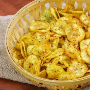 Banana Chips on a wooden basket full of banana chips kept on a handkerchief on wooden surface |