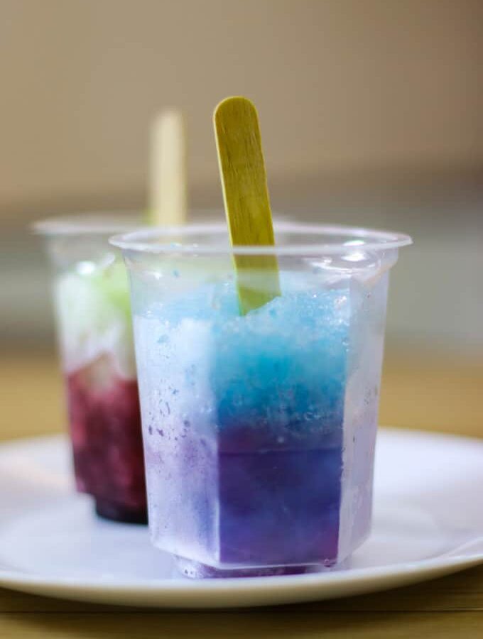 Exotic crushed and tightened ice known as baraf ka gola or Chuski in a white plate with rose syrup and blue lagoon syrup spread over it |