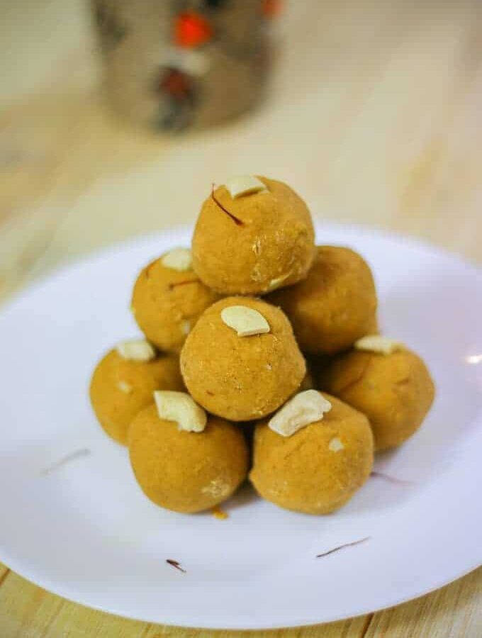 Besan Ke Laddu on a white plate with some cashew and saffron used to garish the laddu kept on a wooden surface