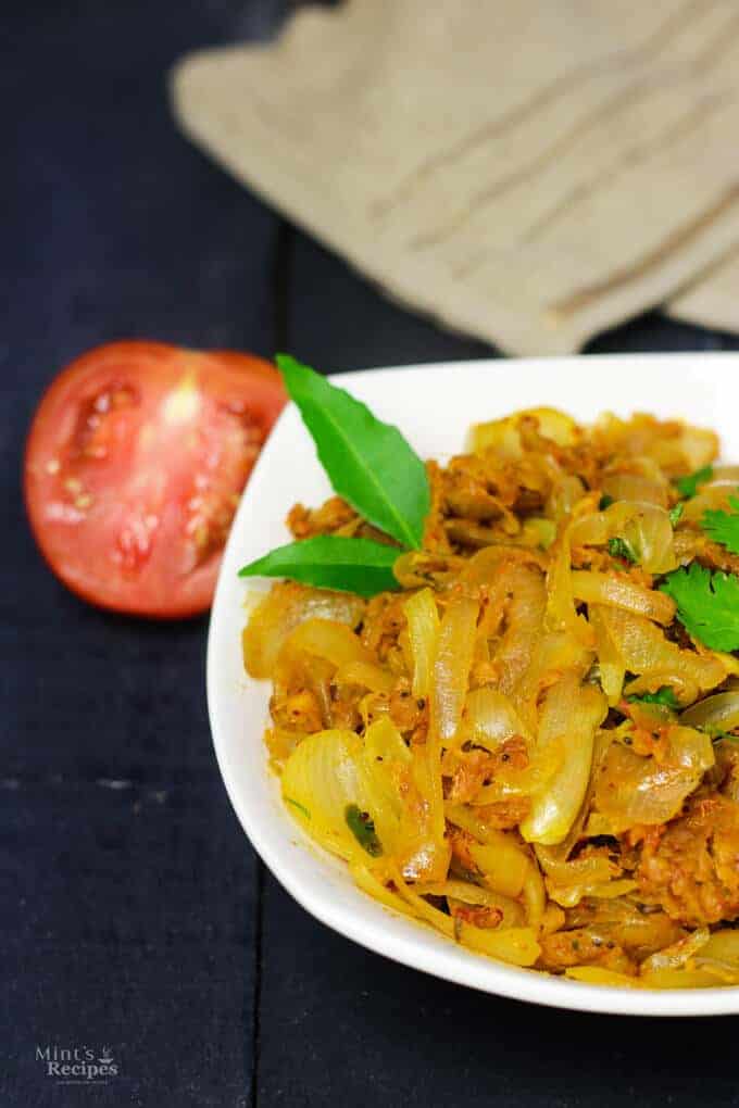 Besan Pyaaz Ki Sabzi on a white bowl full of besan pyaaz ki sabji and garnished with curry leaves kept on a dark wooden surface with and handkerchief on the background 