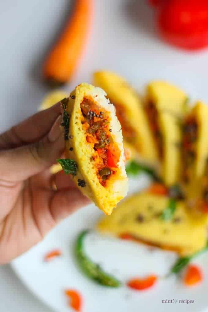 Bread dhokla sandwich on a white plate cutted into pieces in half and tempering of mustard seed and chilli with few strings of curry leaves 