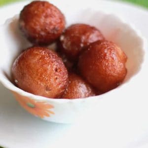 Bread gulab jamun on a white bowl putted on a white plate in a green coloured mat |