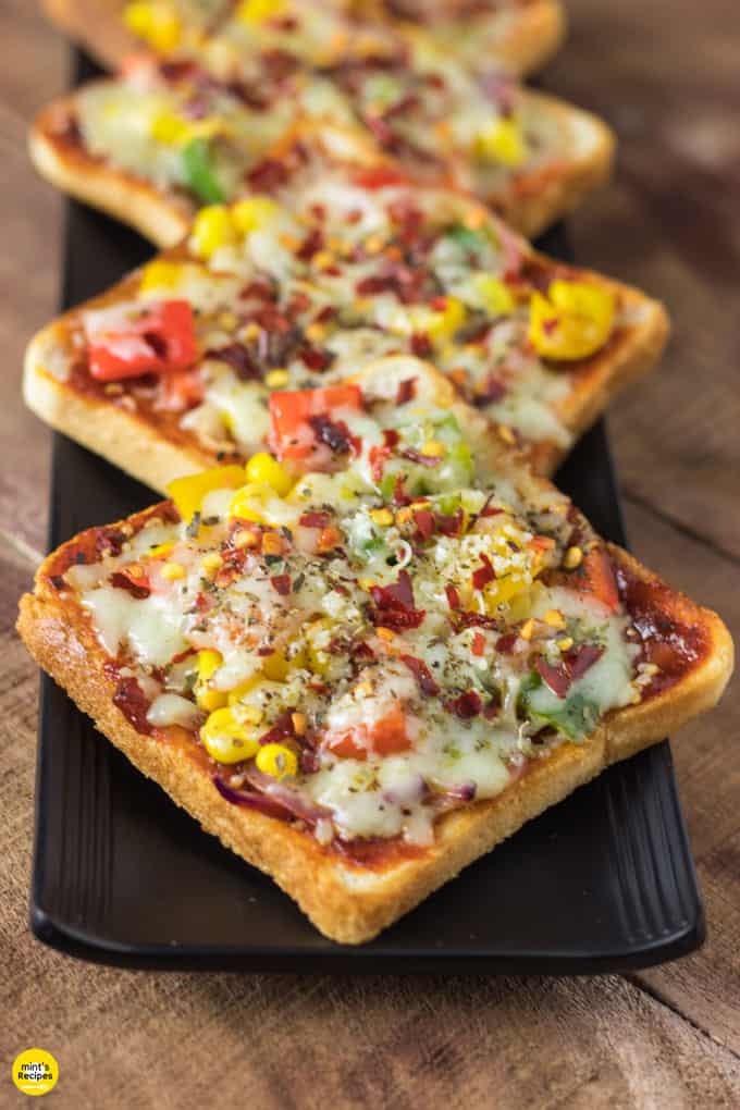 Bread pizza on a black plate with some pieces of bread pizza garnished with some oregano and chilli flakes kept on wooden surface