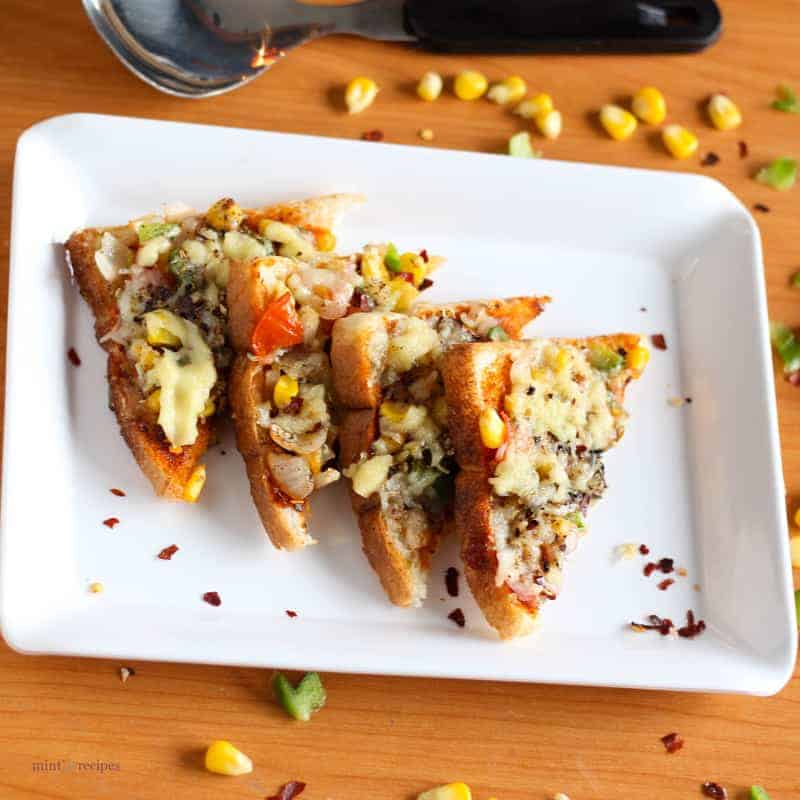 Bread pizza on a black plate with some pieces of bread pizza garnished with some oregano and chilli flakes kept on wooden surface