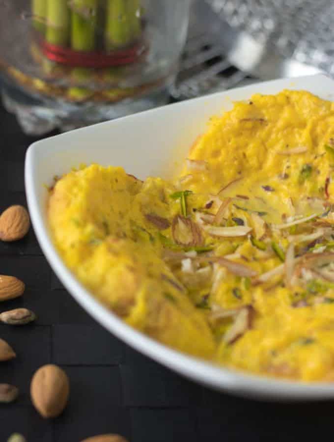 Bread rasmalai on a white bowl garnished with some chopped almonds and pistachios