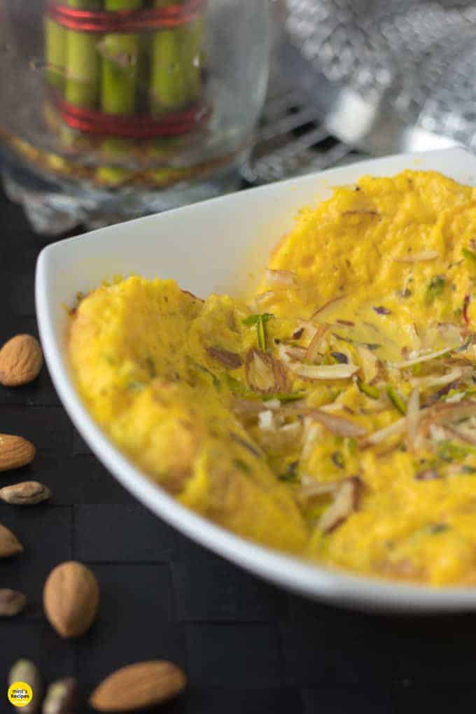 Bread rasmalai on a white bowl garnished with some chopped almonds and pistachios 