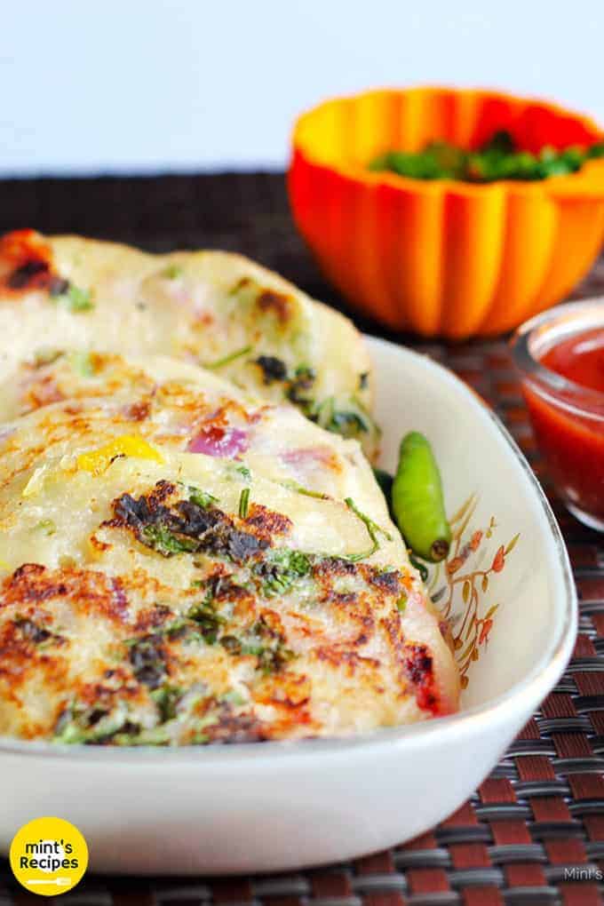 Bread Uttapam On a white bowl with some garnishing of coriander leaves and green chilli, with some green chutney and tomato sauce| 