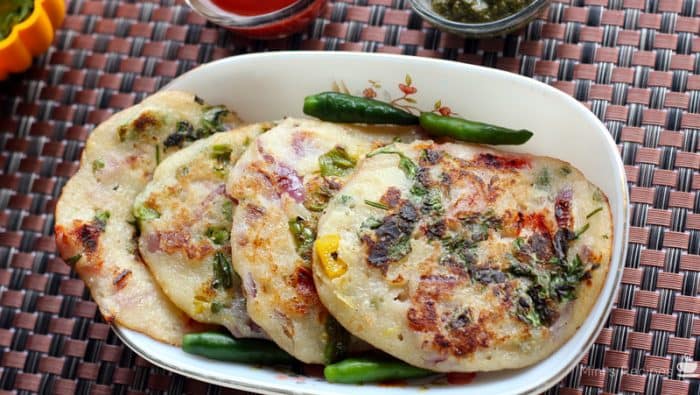 Bread Uttapam On a white bowl with some garnishing of coriander leaves and green chilli, with some green chutney and tomato sauce| www.mintsrecipes.com |