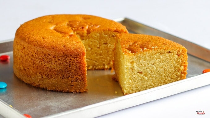 Eggless Vanilla Cake in a black plate with some gems on a white surface |