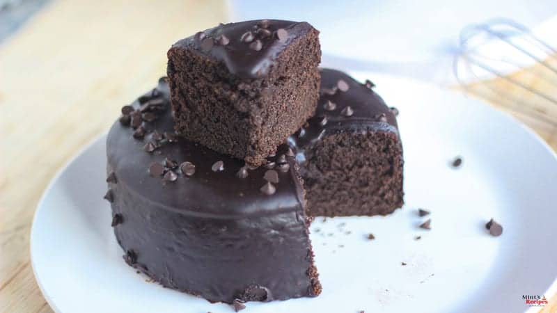 Chocolate Cake with some choco chips sprinkles on a white plate keeped on a wooden surface with a turntable in the background |