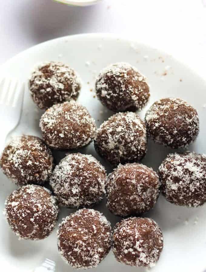Chocolate coconut balls on a white plate with some coconut balls and garnished with some dessicated coconut