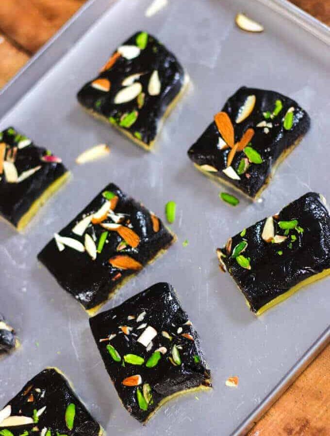 Chocolate Barfi on a steel tray with some pieces of chocolate khoya barfi with some garnishing of pista, and almonds kept on a wooden surface |