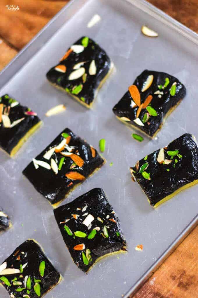 Chocolate Barfi on a steel tray with some pieces of chocolate khoya barfi with some garnishing of pista, and almonds kept on a wooden surface |