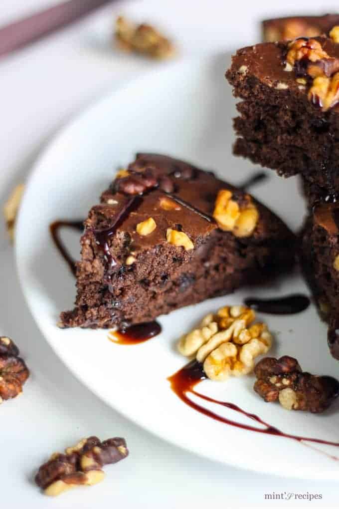 Chocolate Walnut Brownie Recipe on a white plate with some walnuts and chocolate syrup 