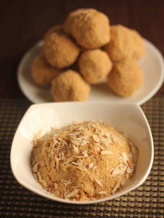 Rajasthani Churma Laddoo on a white plate putted on a mat and a bowl full of churma with some almonds garnished on it |