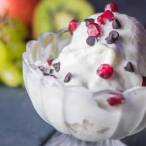 Corn-rasgulla-icecream on a glass bowl with a piece of corn rasagulla in it covered with vanilla icecream and garnished with some choco chips and pomogranate with a dark background |