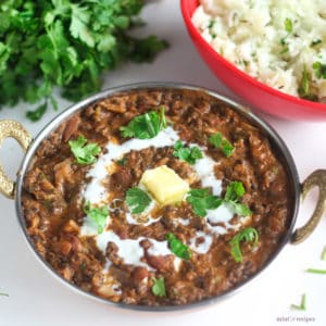 Dal Makhani on a deep heavy pan on a white surface. garnished with butter and cream with some coriander leaves