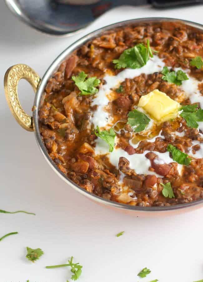 Dal Makhani on a deep heavy pan on a white surface. garnished with butter and cream with some coriander leaves | www.mintsrecipes.com |