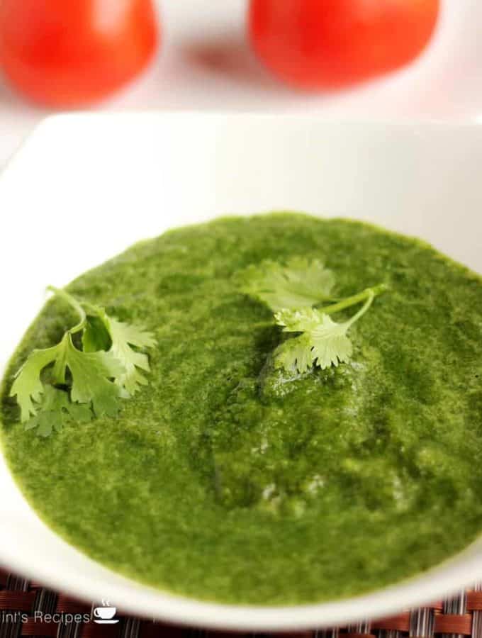 Green chutney dhaniya pudina on a white bowl with some coriander leaves |