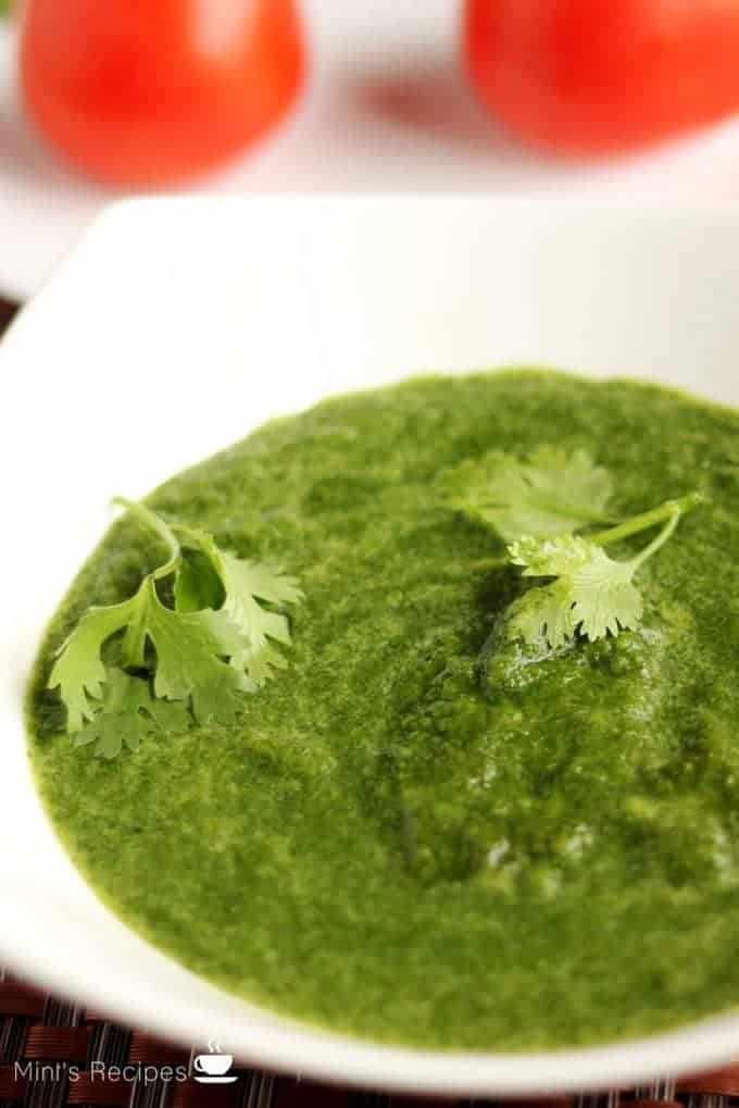 Green chutney dhaniya pudina on a white bowl with some coriander leaves |