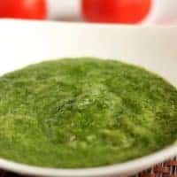 Green chutney dhaniya pudina on a white bowl with some coriander leaves |