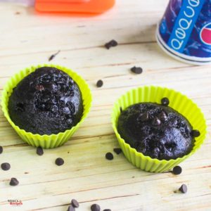 Eggless chocolate cupcake in a silicon mould with some choco chips sprinkles all over it on a wooden surface with a bottle behind |
