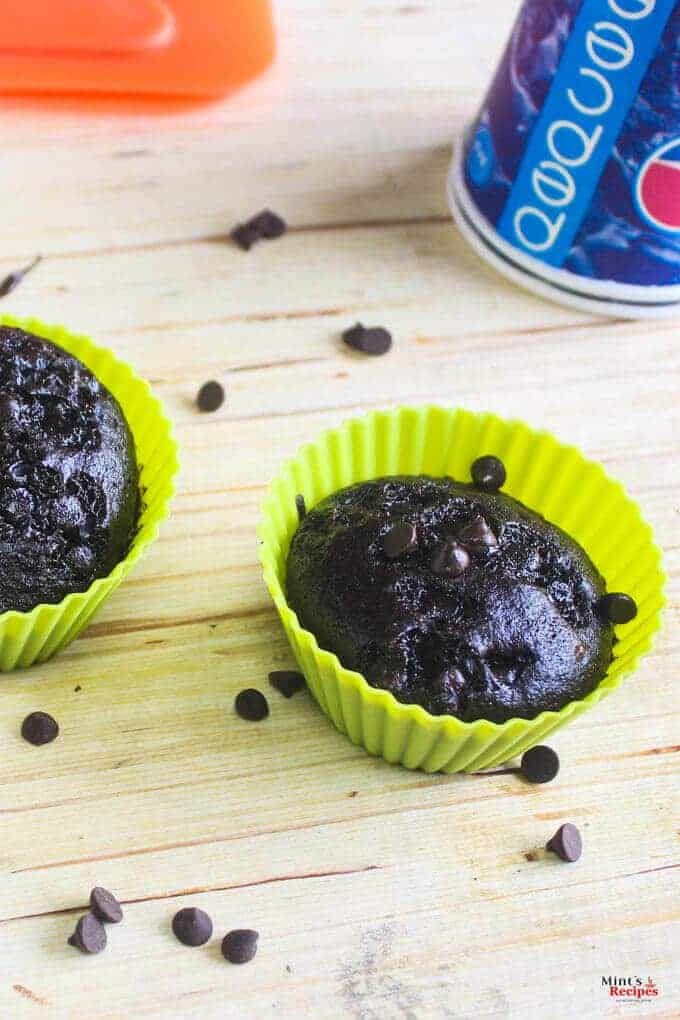 Eggless chocolate cupcake in a silicon mould with some choco chips sprinkles all over it on a wooden surface with a bottle behind |