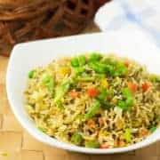 Vegetable fried rice on a white bowl garnish with spring onion on a mat with a dark background|