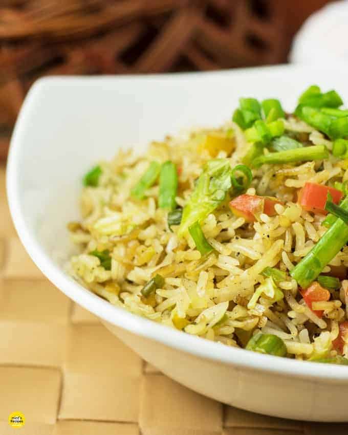 Vegetable fried rice on a white bowl garnish with spring onion on a mat with a dark background|