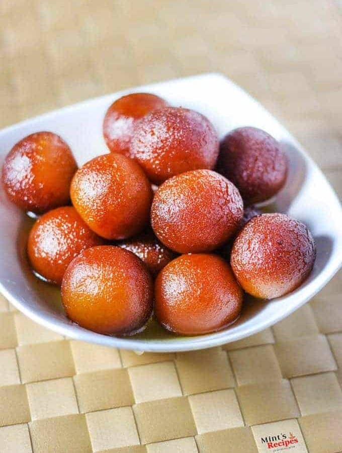 Gulab Jamun on a white bowl with lots of gulab jamun kept on a mattress