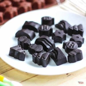 Chocolates on a white plate with a chocolate mould and wire whisker in the background