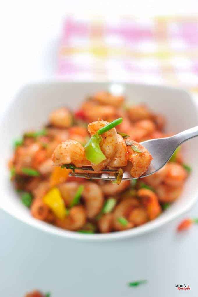 Indian style macaroni in a white bowl, garnished with some spring onion. with a white background and a fork on a hankerchief | 