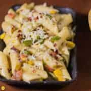 Italian white Sauce Pasta on adisposable black plate with some chilli flakes,italian seasoning and grated cheese with some capsicums on the background |