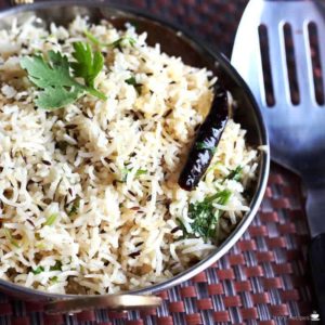 Jeera Rice on a deep vessel garnish with some cilantro on a dark colour mat |