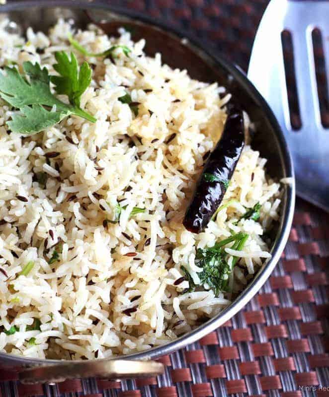 Jeera Rice on a deep vessel garnish with some cilantro on a dark colour mat |