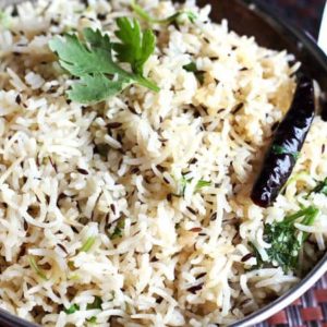 Jeera Rice on a deep vessel garnish with some cilantro on a dark colour mat | www.mintsrecipes.com |