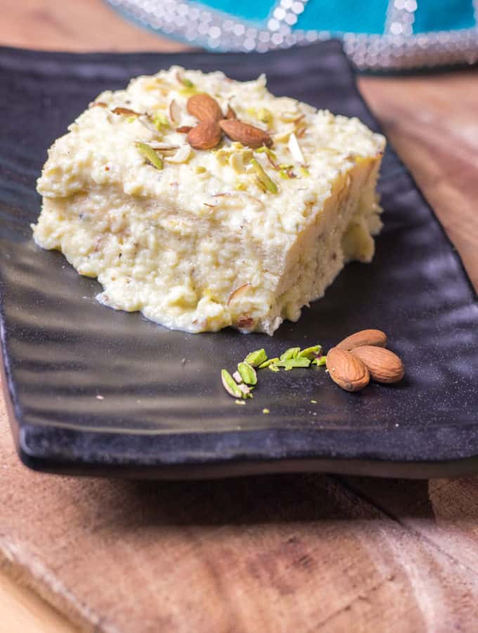 Kesaria Shahi Sandwich on a black tray with some garnishing of pista, almonds and cashew kept on a wooden surface with a basket in the background